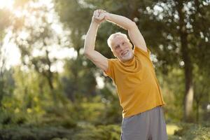 Senior man stretching arms in park during morning exercise photo