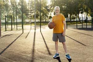 Senior man holding basketball on outdoor court at sunset photo