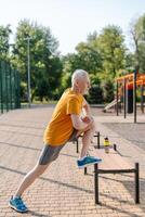 Senior man stretching legs on bench in park before workout photo