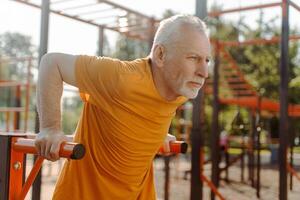 Senior man doing dips on parallel bars in outdoor gym for fitness and wellbeing photo