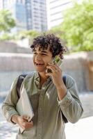Cheerful university student walking outdoors and talking on smartphone photo