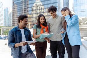 Group of young professionals collaborating outdoors on a project using digital tablet and notebook photo