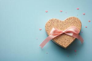 Heart shaped gift box with pink ribbon on a light blue background adorned with elegant touches photo