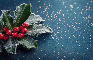 Frosted holly leaves with red berries placed on a shimmering blue background during winter photo