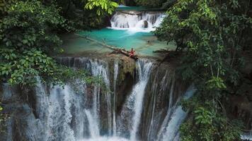 Traveller woman on cascade waterfalls with blue water in Sulawesi. Scenic waterfall in Luwuk, drone view video