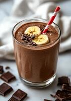Decadent chocolate banana smoothie topped with chocolate pieces and a striped straw photo