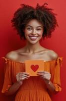 Woman in an orange dress holding a red heart card against a vibrant red background photo
