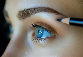Close up of a person applying eyebrow pencil in soft lighting with striking blue eyes photo
