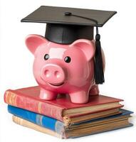 A cheerful piggy bank wearing a graduation cap rests atop a stack of colorful books photo