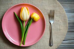 Colorful tulips arranged on a pink plate with a fork, featuring a rustic wooden background photo