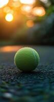A solitary tennis ball resting on a court as the sun sets in the background during twilight photo