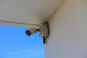 A Surveillance Camera Mounted on a Wall Overlooking a Clear Blue Sky, Capturing Moments in an Outdoor Setting With a Hint of Tranquility photo