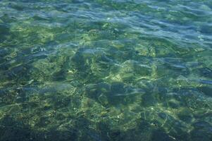 Clear, blue water ripples over rocks in the shallows of a lake photo