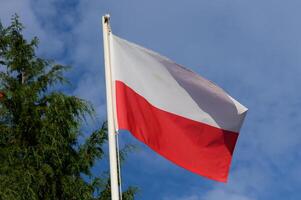 Polish flag waving proudly against a bright blue sky adorned with scattered clouds photo