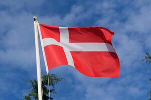 Waving Danish national flag against a backdrop of blue sky and fluffy clouds during a sunny day in Denmark photo