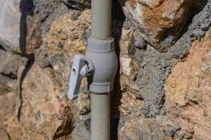 A close-up of a gray valve attached to a stone wall, reflecting sunlight in a tranquil outdoor setting photo