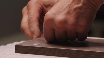 Close-up of man inserts screw into board. Creative. Man screws screw into wooden board. Worker screws screw into board and takes it away video