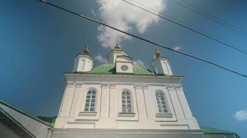 Beautiful view of church with green domes. Clip. Circle around beautiful white church with domes on background sky. Timelapse of church review on background of blue sunny sky with clouds video