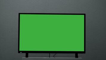 Plasma TV with green screen stands on background wall. Concept. Green-screen TV stands on background gray wall. Green screen TV for inserting chromakey video