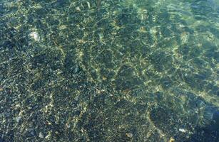Gentle Waves Lap Over Smooth Pebbles in a Tranquil Shallow Lagoon Under the Bright Sunlight photo