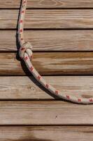 A close-up view of a taut rope with red markings coiled around wooden planks, bathed in warm sunlight on a tranquil afternoon photo