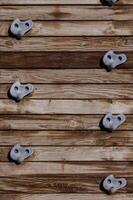Climbing wall with textured holds against wooden backdrop on a sunny day in an outdoor fitness park photo