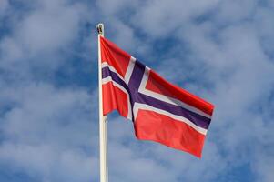 Norwegian flag proudly waving under a bright blue sky with fluffy clouds during a sunny day in Norway photo