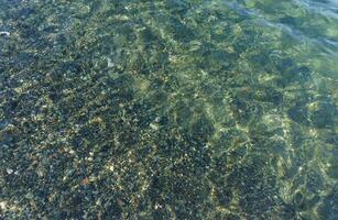 Serene Underwater Landscape Revealing Pebbles and Rippling Shadows on a Clear Water Surface at a Tranquil Beach Location photo