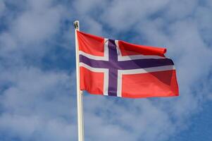 The vibrant Norwegian flag billowing against a backdrop of soft clouds on a bright sunny day in Norway photo