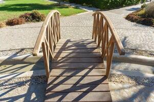 A rustic wooden bridge with unique shadow patterns in a serene garden setting during daylight. photo