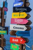 Colorful directional signs point to far-off destinations with an ocean backdrop near a vibrant beach resort during the sunny day photo