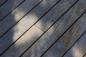 Sunlight filtering through trees casts gentle shadows on weathered wooden planks in a serene outdoor setting photo