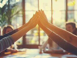 Diverse group of hands reaching together in a collaborative gesture, symbolizing teamwork and unity in a modern office setting with sunlight streaming through large windows. photo