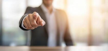 A business professional confidently points forward, symbolizing leadership and direction. The background is softly blurred, suggesting a modern office environment. photo