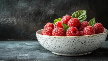 A vibrant bowl filled with fresh raspberries garnished with green mint leaves, set against a dark textured background, showcasing the rich color and freshness of the fruit. photo