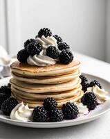 A stack of pancakes topped with whipped cream and blackberries photo