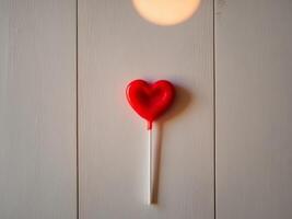 A red heart shaped lollipop on a wooden surface photo
