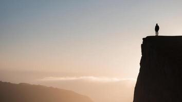 Silhouette of a man standing on the edge of a cliff at sunset photo