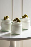Three jars of yogurt with olives on a white table photo