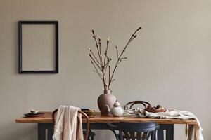 Stylish rustic interior of dining room with walnut wooden table, retro chairs, decoration, dried flower and mock up picture frame in minimalist home decor. photo