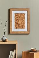 Minimalist composition on wooden shelf with brown mock up poster frame, dried flower in vase, cube, book, cup of coffee and elegant personal accessories in home decor. Template. photo