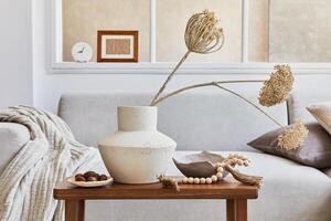 Creative composition of stylish and cozy living room interior with mock up frame, grey sofa, window, dried flowers in vase and personal accessories. Beige neutral colors. Details. photo