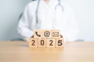 Contact Us concepts. Happy New Year 2025 with Wood block of Email, call Phone and Website Address sign against Doctor background. Healthcare Customer support hotline, health and communication concept photo