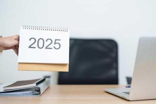negocio mujer cambio 2025 año calendario en mesa con ordenador portátil computadora durante trabajando y escritura en oficina. cuenta regresiva, contento nuevo año, resolución, año final y nuevo comienzo y metas plan acción concepto foto