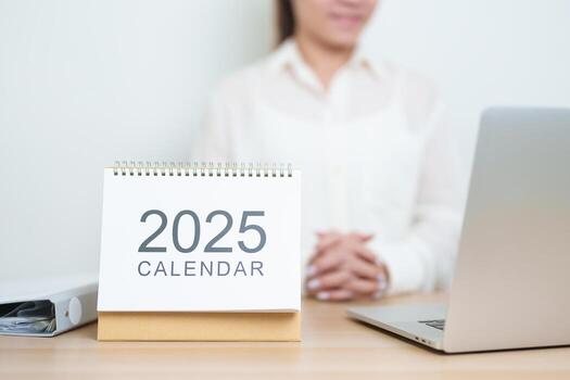 2025 Year Calendar on table with business woman using laptop computer, working and writing in office. countdown, Happy New Year, Resolution, Year End and New Start and Goals Plan Action Concept photo