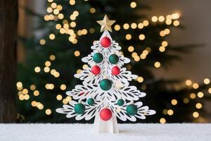 White christmas tree decoration standing on snowy surface with blurred christmas tree in background photo