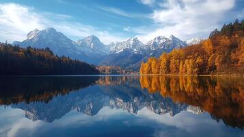 Snowy mountains reflecting in calm lake with autumnal trees photo