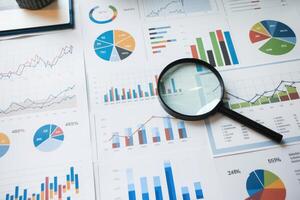 Magnifying glass analyzing business charts and graphs for market research and financial data analysis photo