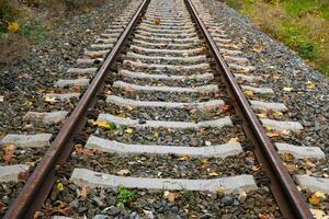 View of Railroad tracks stretching into the distance. Rails and sleepers are covered in rust and partially hidden by fallen leaves. Low viewpoint, industrial style. Blurred background photo