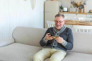 mayor hombre compras en línea participación teléfono inteligente pago con crédito tarjeta. antiguo abuelo comprando en Internet entrar crédito tarjeta detalles. en línea compras entrega Servicio más viejo Generacion moderno tecnología uso foto